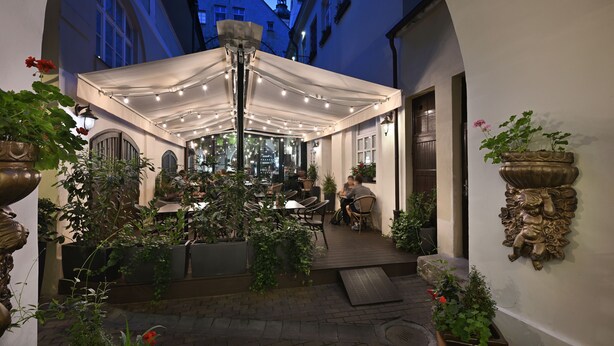 An outdoor café with tables and chairs, surrounded by potted plants and a white canopy. - Little King Hotel U Malvaze (Prague)