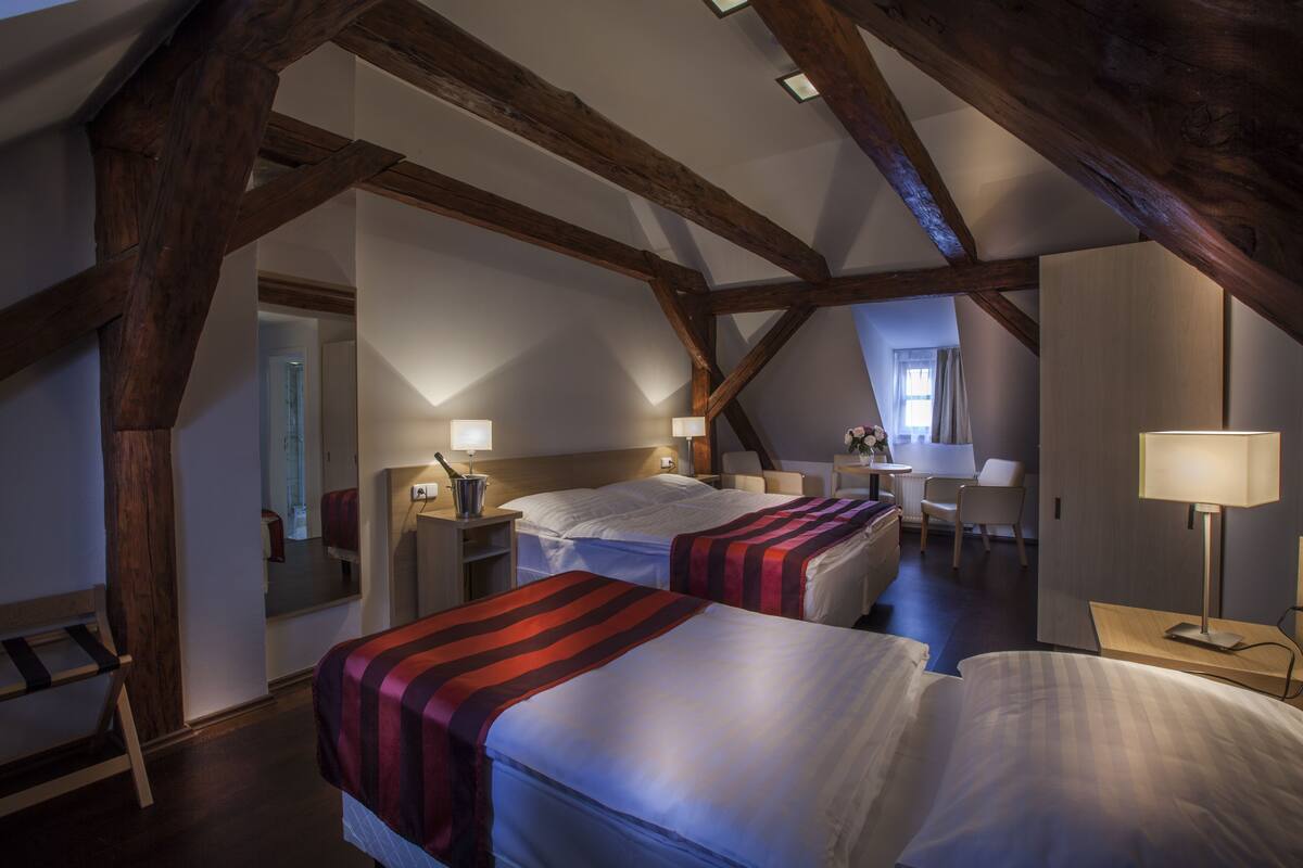 A hotel room with two beds, wooden beams, a desk, and a chair.