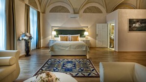 A spacious bedroom with a large bed, two bedside tables with lamps, a decorative rug, and a chandelier. - Little King Hotel U Malvaze (Prague)