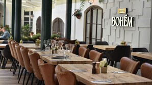 An outdoor dining area with wooden tables and leather chairs, a sign reading "BOHEM", and a wall with a geometric pattern. - Little King Hotel U Malvaze (Prague)