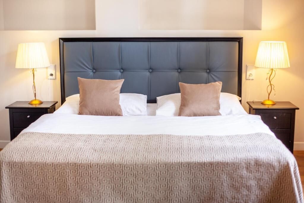 A neatly made bed with a patterned bedspread, a tufted headboard, and two bedside lamps on matching nightstands.