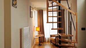 Eine Treppe mit Holzboden und schwarzen Geländern, ein Heizkörper, ein Tisch mit Lampe und ein Stuhl in einem Raum mit beigen Wänden und einem Fenster mit Vorhängen.