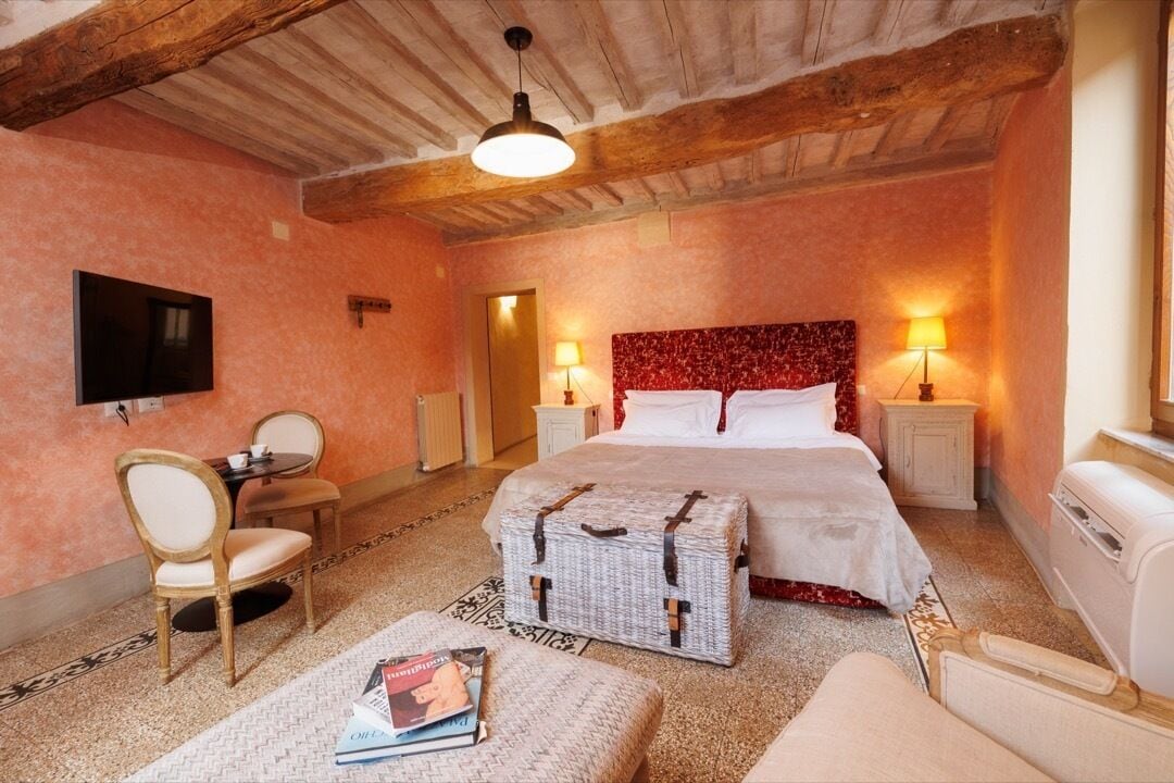 Ein Schlafzimmer mit einem Bett, Nachttischen, einem Sessel, einem Fernseher und einem kleinen Tisch mit einer Lampe.