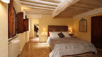A bedroom with a bed, wooden ceiling beams, patterned floor, and a nightstand with a lamp.