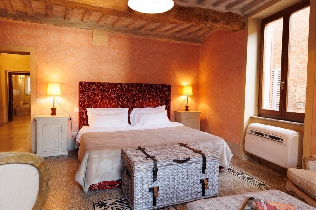 A bedroom with a large bed, two bedside lamps, a radiator, and a window.
