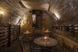 A wine cellar with stone walls, wine racks, and tables with glasses and candles. - Il Battistero Siena - Residenza d'Epoca (Siena)