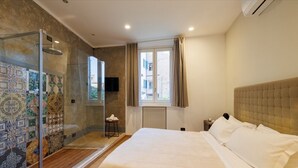 Ein Schlafzimmer mit einem großen Bett, einer Duschkabine aus Glas, einem Fernseher und einem Fenster mit Vorhängen.