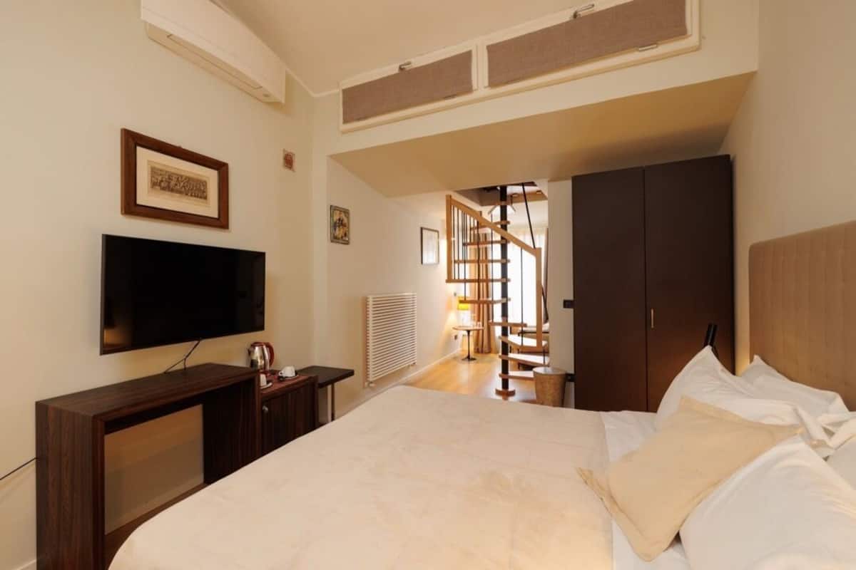 A bedroom with a bed, a TV, a wardrobe, and a staircase leading to another room.