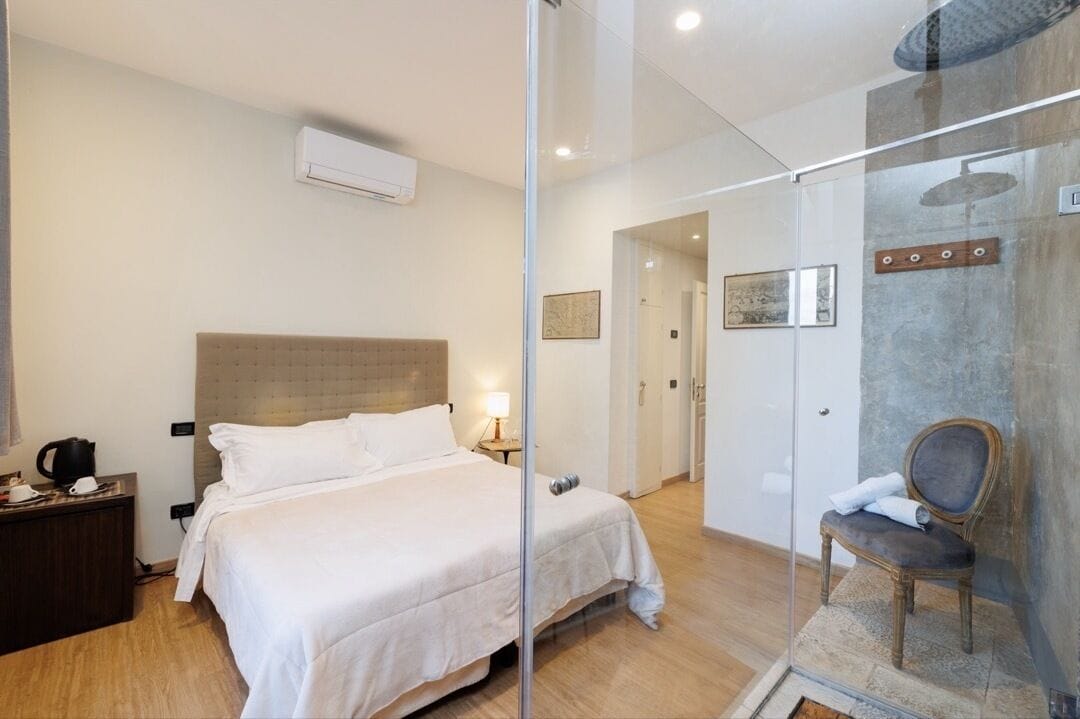 Quarto de hotel com cama, mesa de cabeceira, cadeira e área de chuveiro.