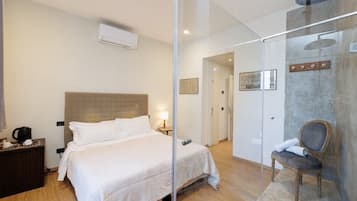 Quarto de hotel com cama, mesa de cabeceira, cadeira e área de chuveiro.