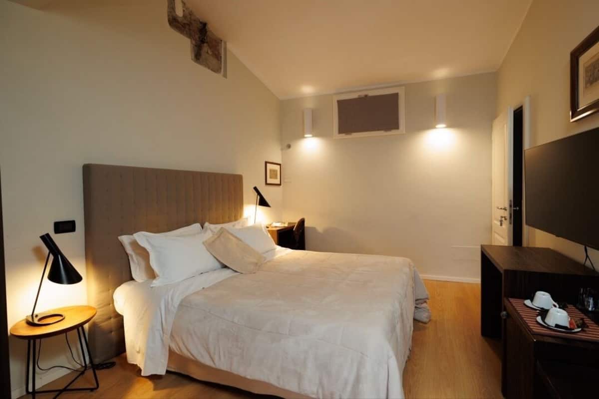 A hotel room with a bed, bedside tables, a TV, and a wall-mounted light fixture.