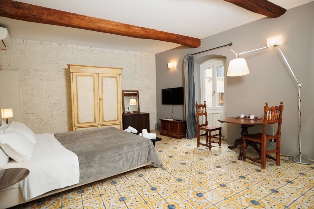 Een slaapkamer met een bed, een houten garderobe, een bureau met stoel, een staande lamp en een televisie.