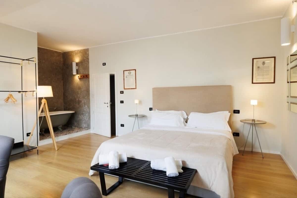 A hotel room with a bed, bedside tables, a bench, a bathtub, and a wall-mounted towel rack.