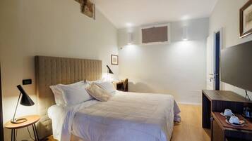 Quarto com cama, mesa de cabeceira, luminária, TV e pequena mesa de madeira.