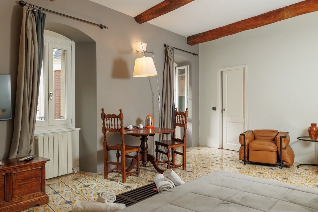 A room with a bed, a wooden table with chairs, a small sofa, a lamp, and a window with curtains.