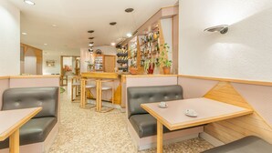 Un café acogedor con mesas de madera y asientos con cojines, una zona de bar con estanterías llenas de botellas y un suelo de baldosas.