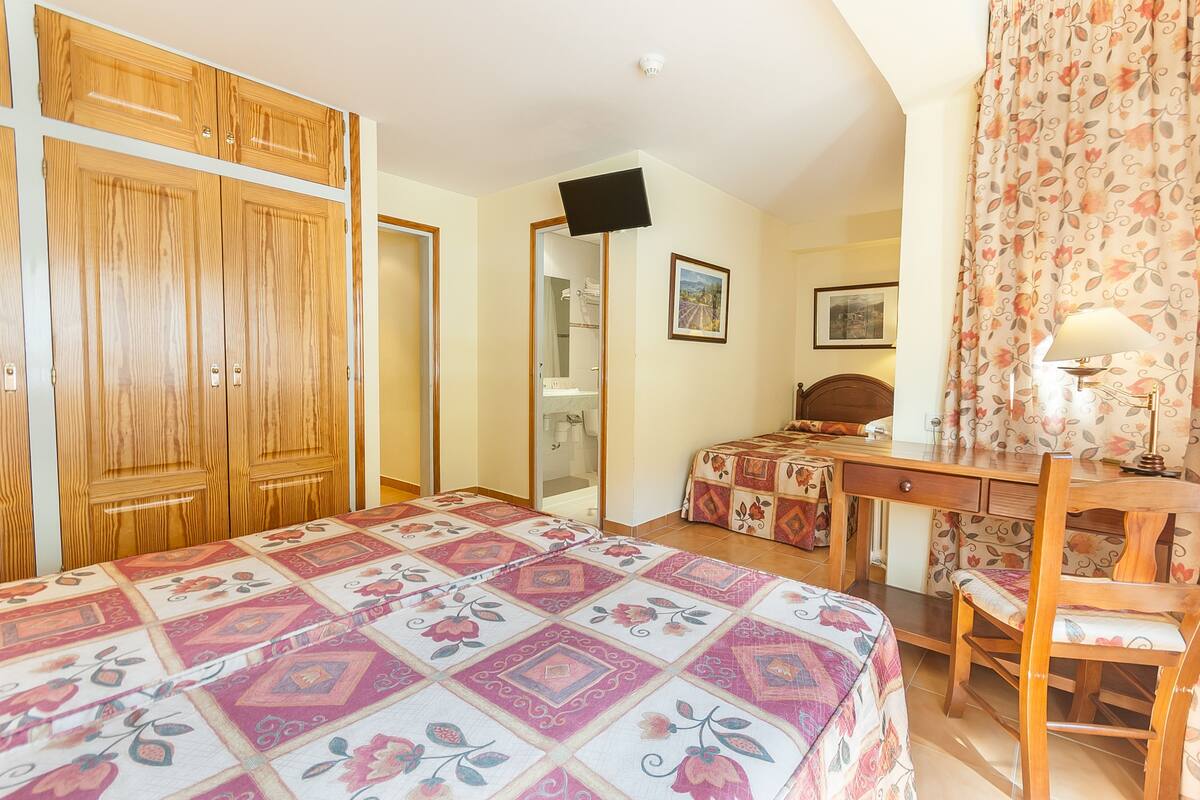 Quarto com cama, escrivaninha, cadeira, guarda-roupa e televisão.