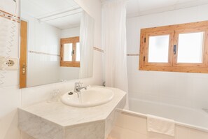 A bathroom with a white sink, mirror, and wooden-framed window. - Hotel Montecarlo (Encamp)