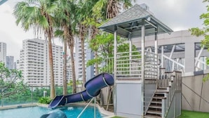 A swimming pool with a slide, surrounded by palm trees and modern buildings in the background. - 39 Boulevard Executive Residence (Bangkok)