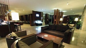 A modern hotel lobby with a curved seating area, a central coffee table, and a television.