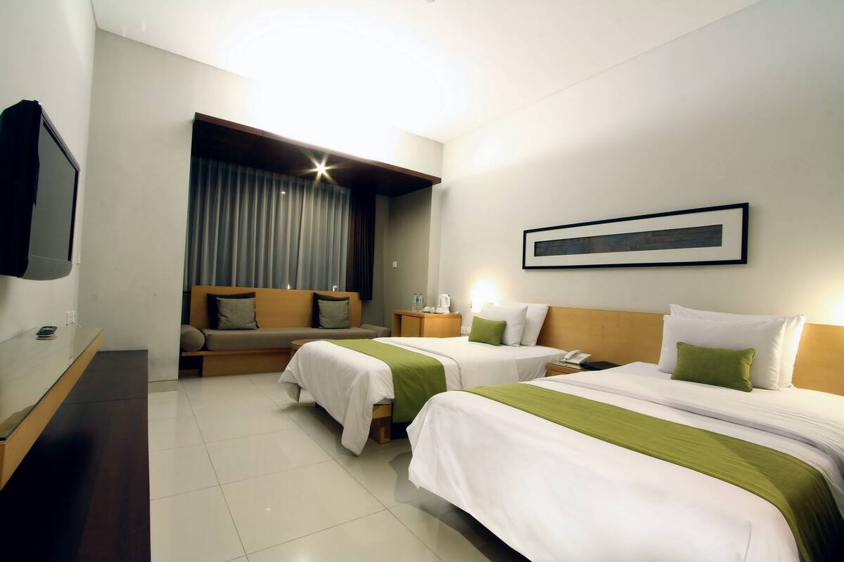 A hotel room with two beds, a sofa, a TV, and a framed picture on the wall.