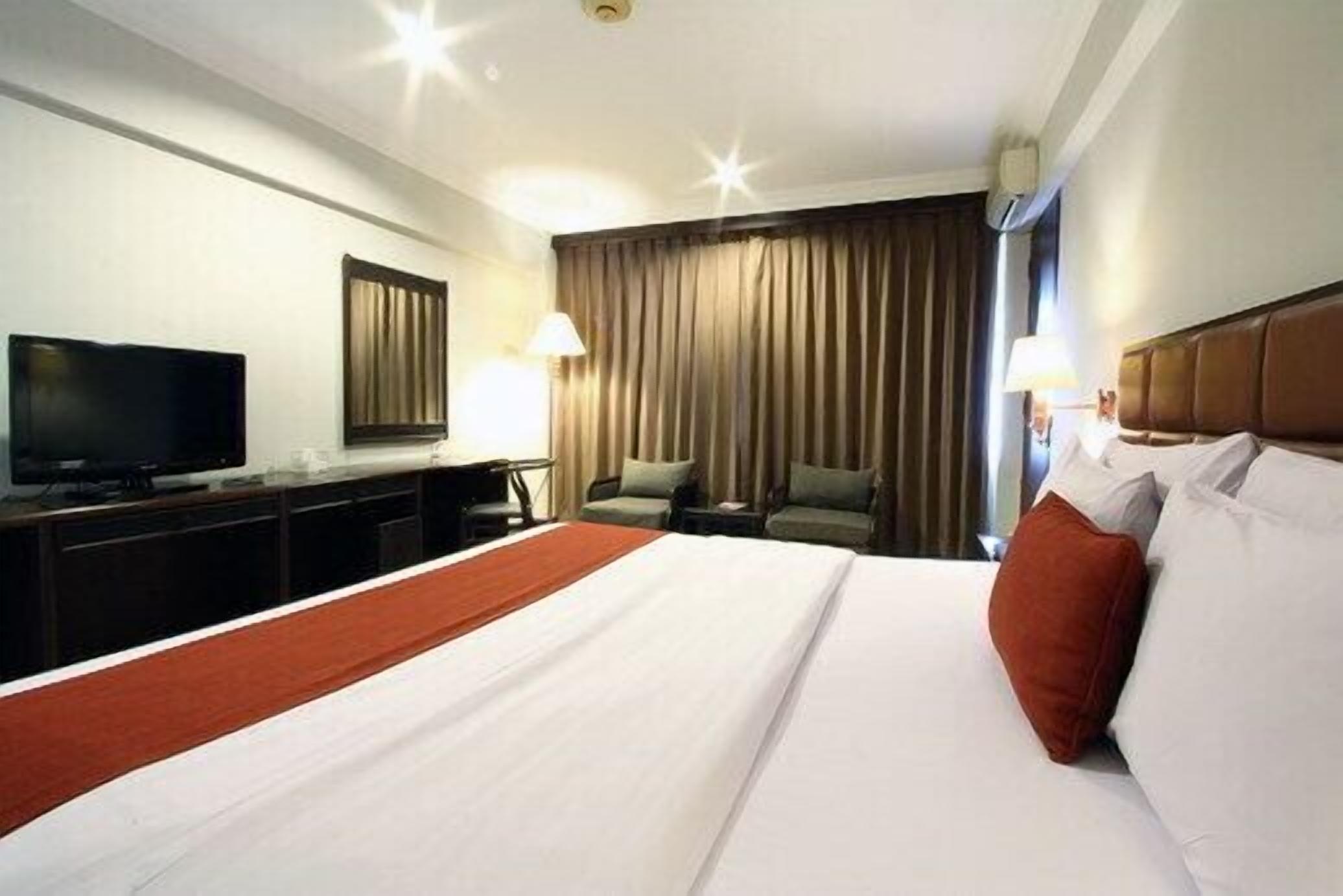 A hotel room with a large bed, a television, a desk, and a chair.