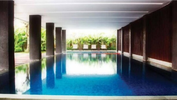 A swimming pool with clear blue water, surrounded by columns and a view of greenery.