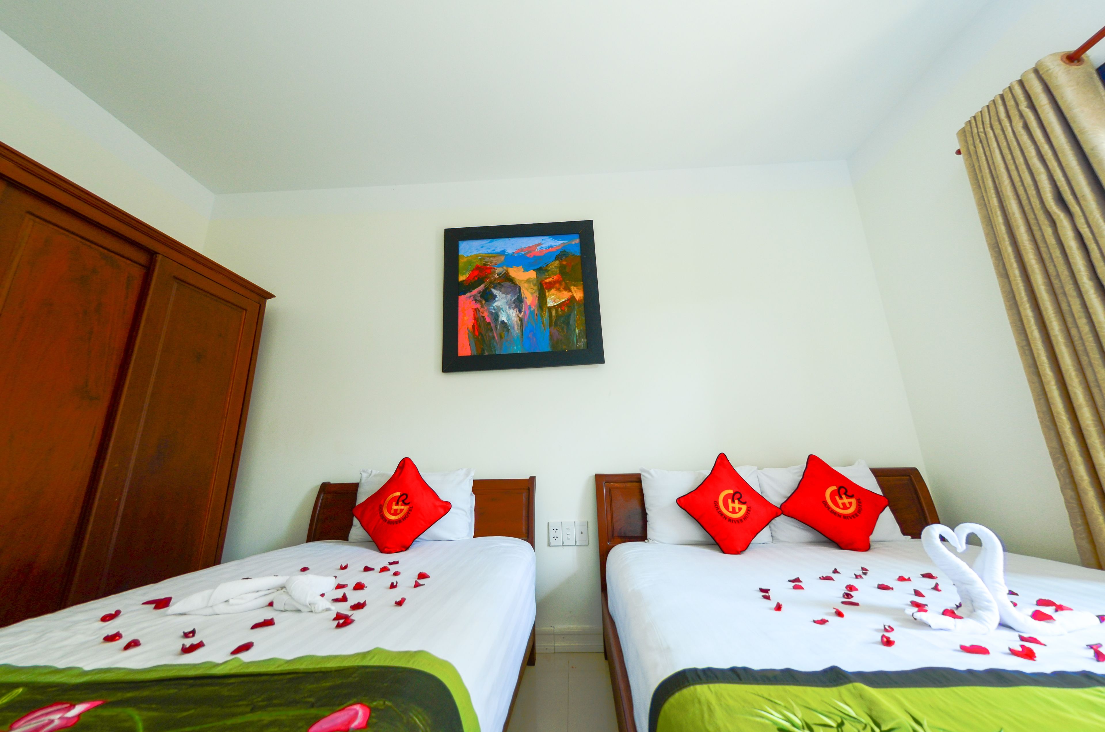 Habitación de hotel con dos camas, cada una con almohadas rojas y una disposición de toallas con forma de corazón.