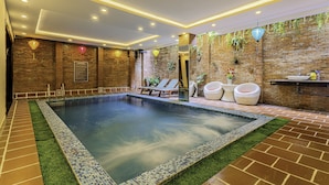 A modern indoor pool area with a brick wall, lounge chairs, and a small hot tub. - Golden River Hotel (Da Nang)