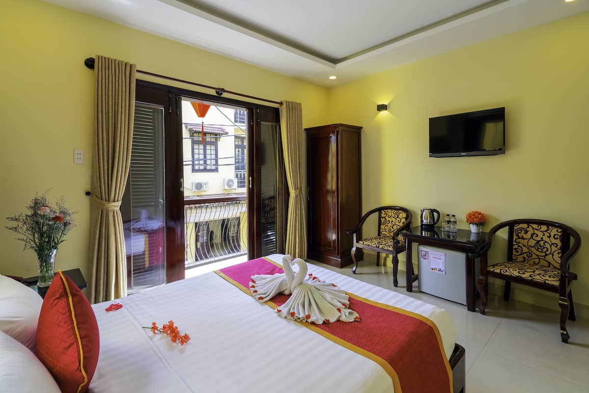 Una habitación de hotel con una cama, dos sillas, un televisor y un escritorio con un florero.