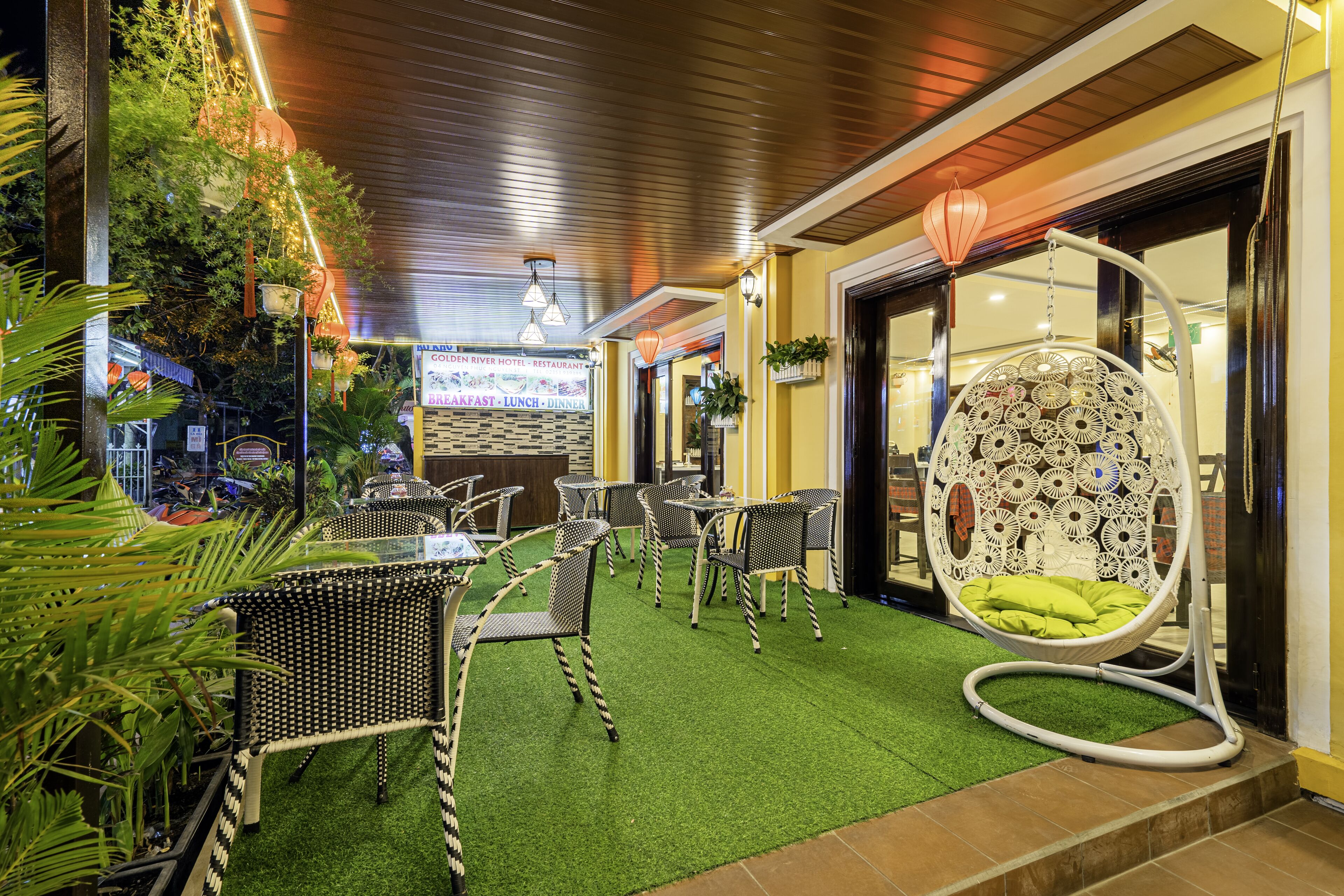 An outdoor seating area with tables and chairs, a hanging chair, and potted plants.