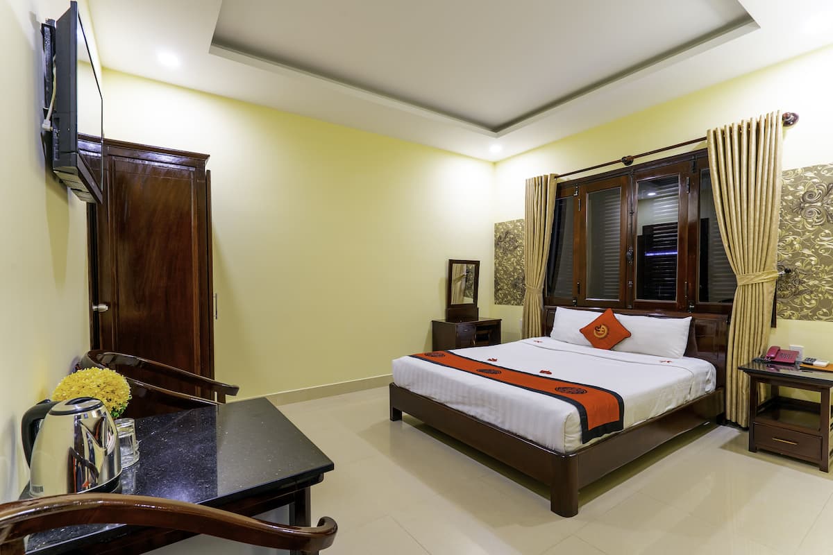 Una habitación de hotel con cama, mesita de noche, silla y escritorio con tetera y flores.