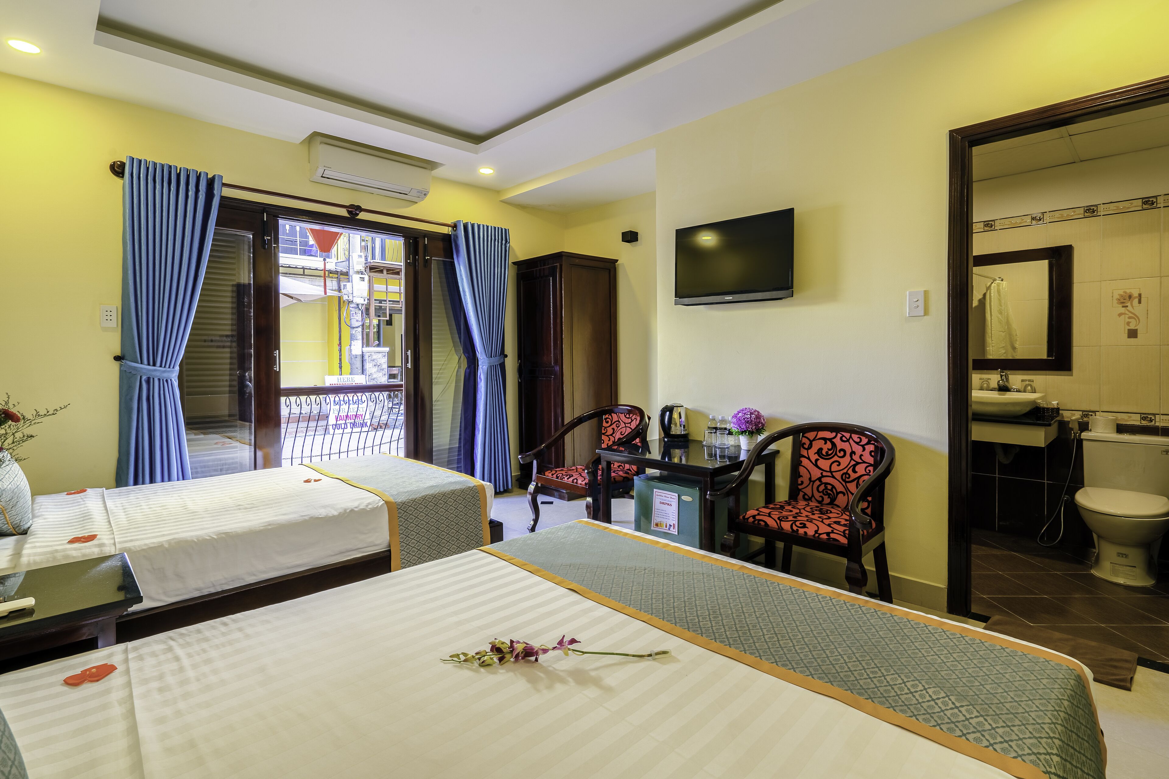 A hotel room with two beds, a desk with a chair, a TV, and a bathroom visible through an open door.