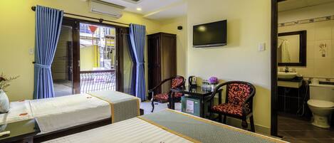 Une chambre d’hôtel avec deux lits, un bureau avec une chaise, une télévision et une salle de bain visible à travers une porte ouverte.