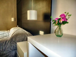 A modern hotel room with a bed, a white bedside table, a vase with flowers, and a pendant light. - Dea Roma Inn (Rome)
