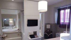 A modern bathroom with a large bathtub, a toilet, and a sink. There is a television mounted on the wall and a small table with a lamp. - Dea Roma Inn (Rome)