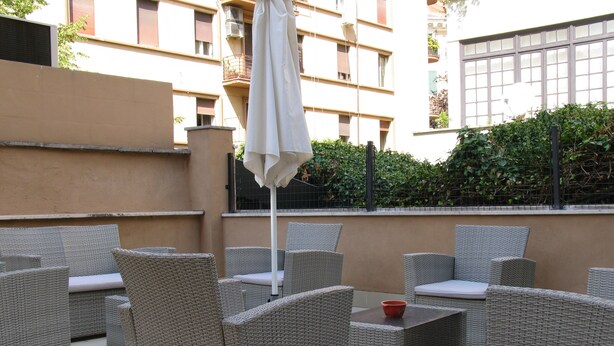 An outdoor patio area with wicker furniture and a white umbrella. - Dea Roma Inn (Rome)