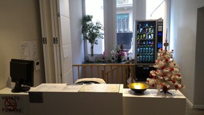 A hotel reception area with a desk, a computer, a vending machine, a Christmas tree, and a window with a balcony view. - Dea Roma Inn (Rome)