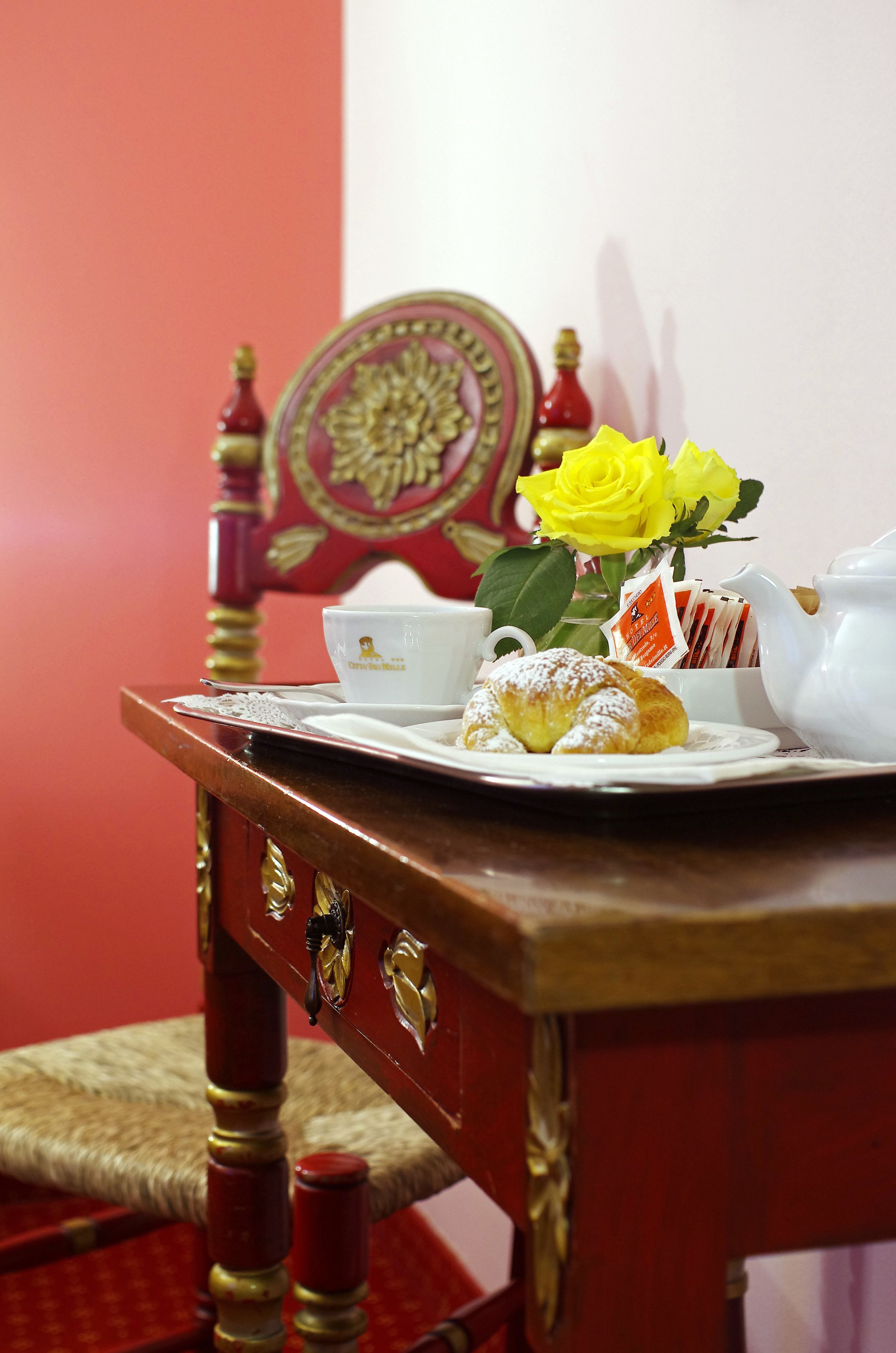 A table with a teapot, a cup, a plate with pastries, and a yellow rose.