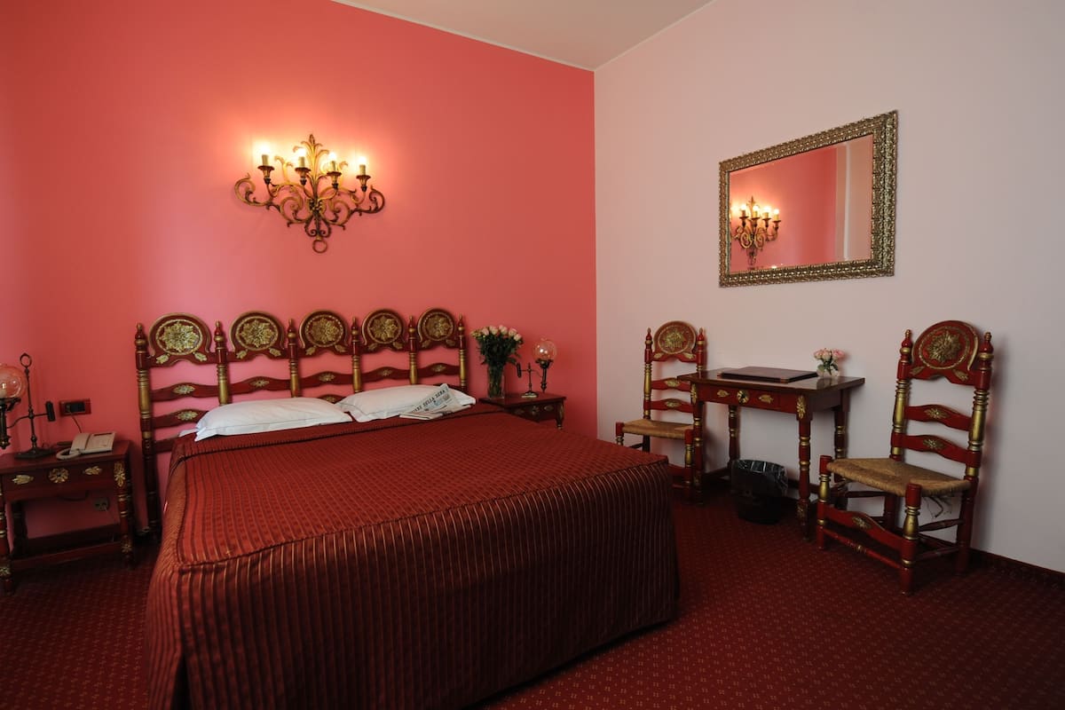 Una habitación con una cama grande, una mesita de noche, una silla, un escritorio y un espejo.