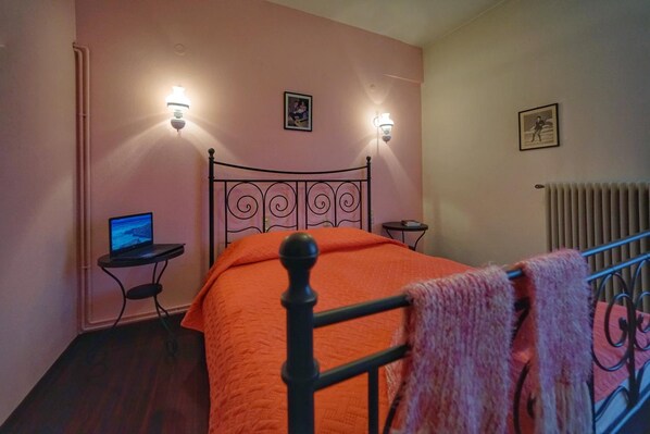 A bedroom with a bed, two wall-mounted lamps, a laptop on a side table, and a radiator.