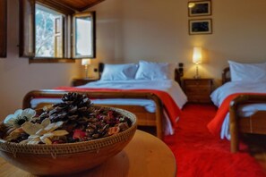 A hotel room with two beds, a wooden headboard, a red carpet, and a bowl of dried flowers on a table.