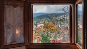 Una habitación con marco de ventana de madera, vista a un pueblo con edificios de tejados rojos y un árbol con hojas otoñales.