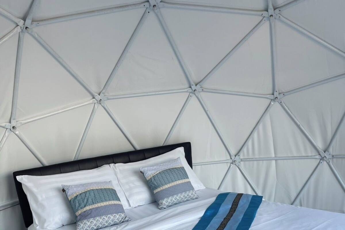 Ein ordentlich bezogenes Bett mit weißer Bettwäsche und einer blau gestreiften Decke, vor einer Wand mit geometrischen Mustern.