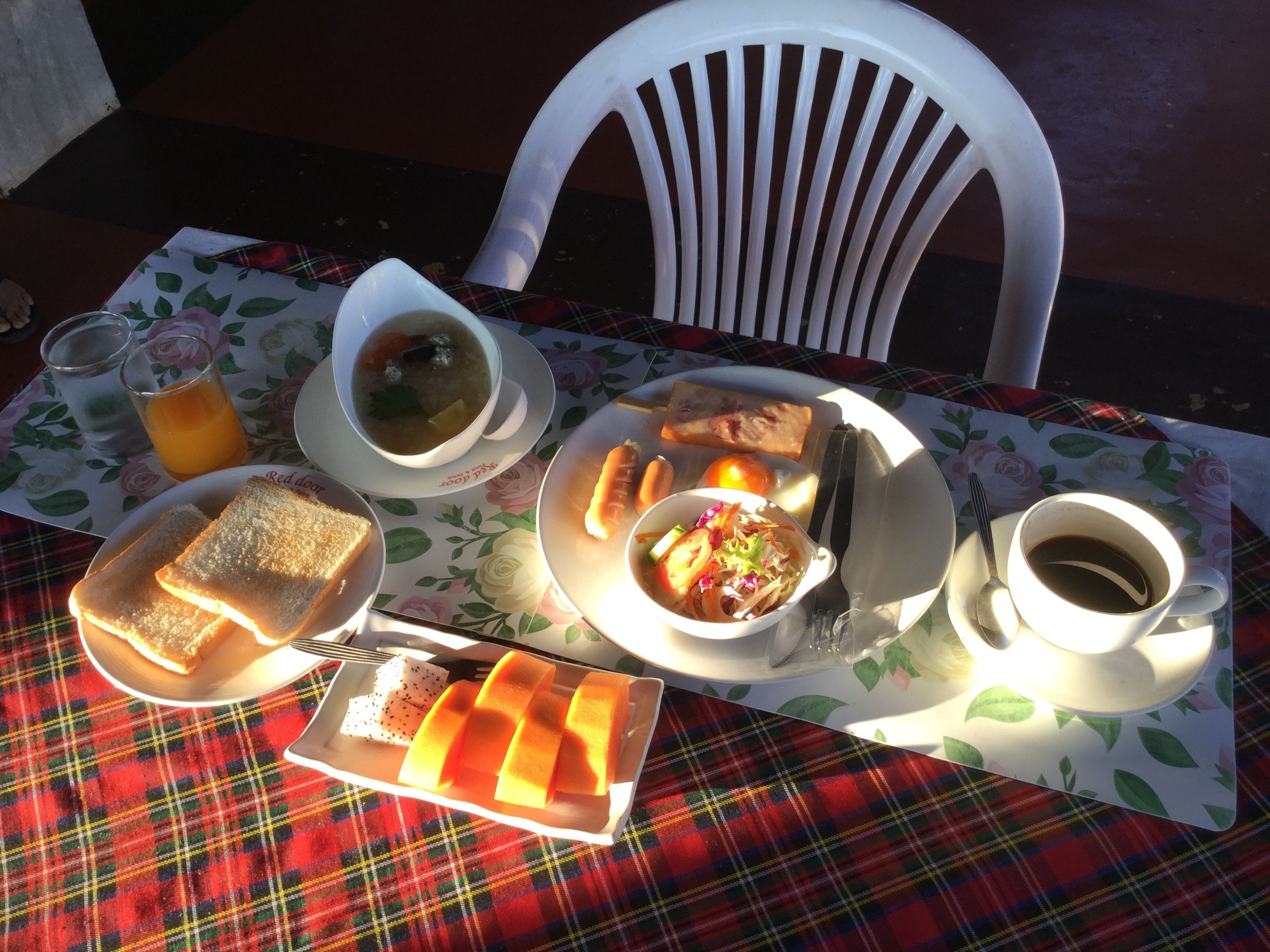 Mesa posta com uma refeição que inclui sopa, pão, uma salada de frutas e uma xícara de café, sobre uma toalha de mesa xadrez.
