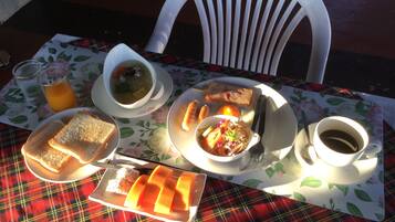 Mesa posta com uma refeição que inclui sopa, pão, uma salada de frutas e uma xícara de café, sobre uma toalha de mesa xadrez.