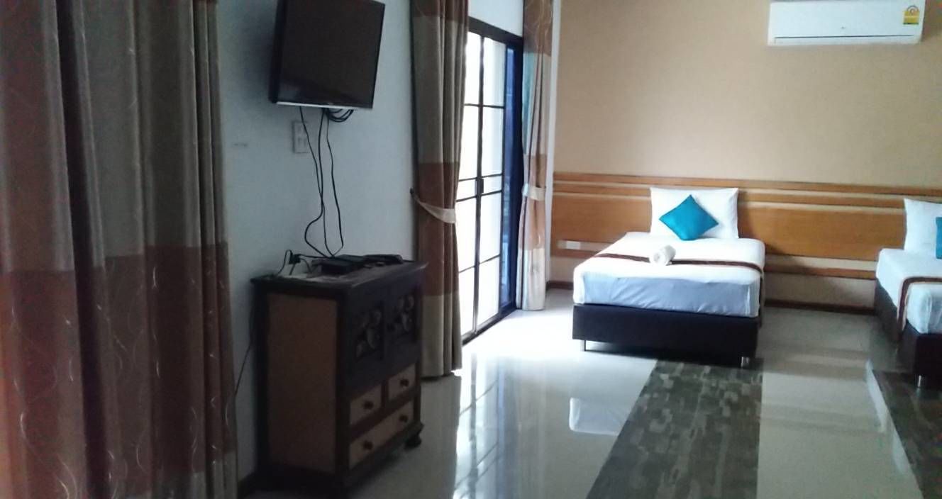 A hotel room with a bed, a TV mounted on the wall, a dresser, and a window with curtains.