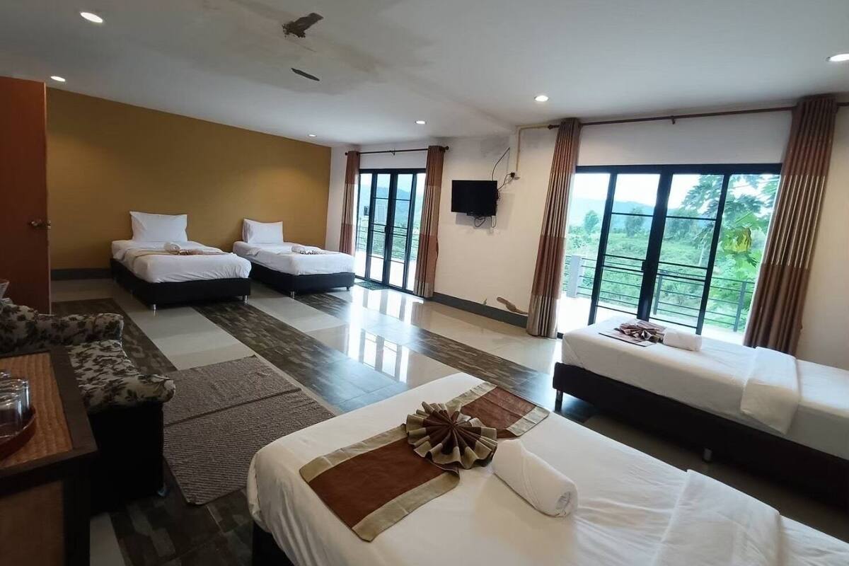 Ein Hotelzimmer mit zwei Einzelbetten, einer Schlafcouch, einem Fernseher und großen Fenstern mit Blick ins Freie.