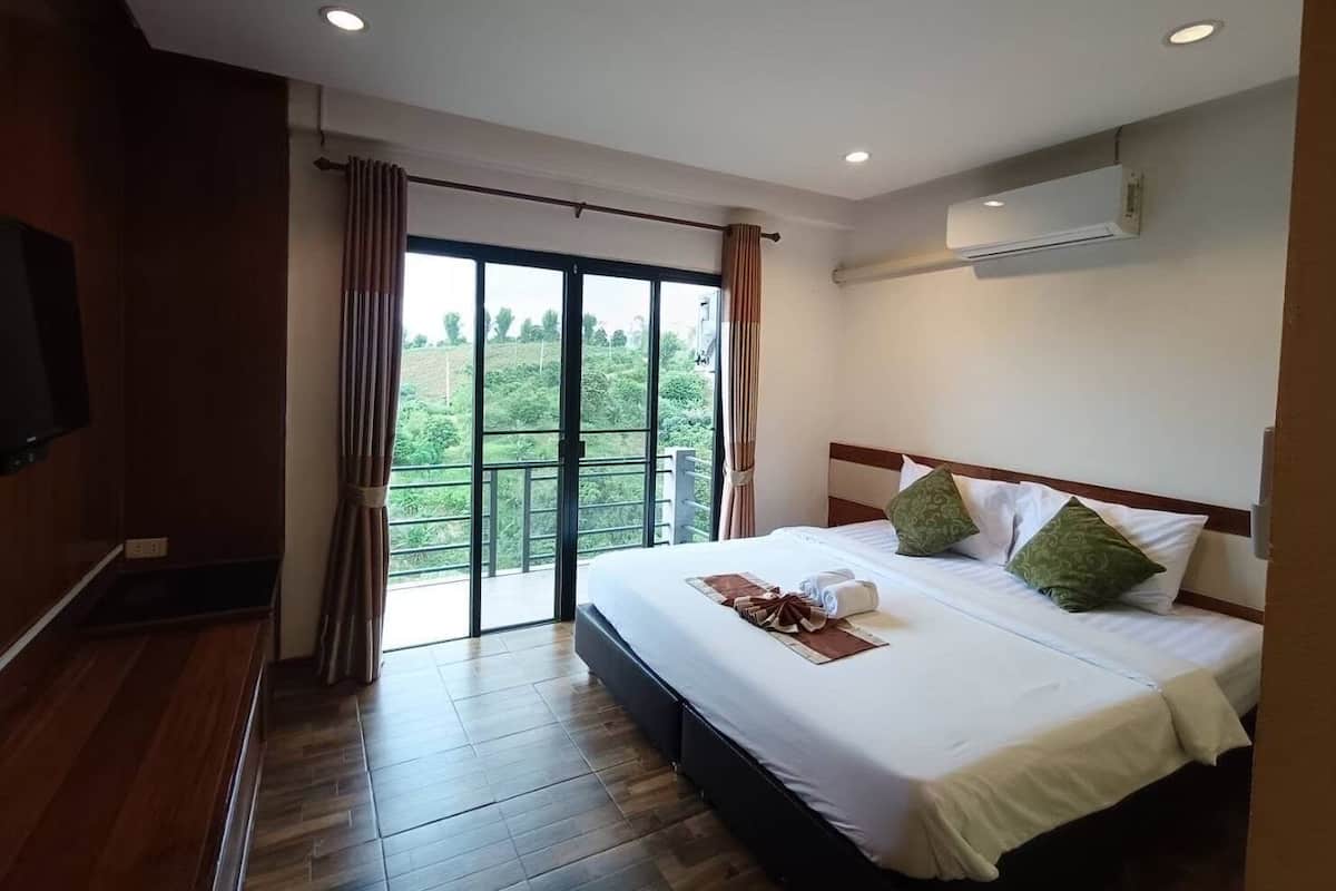 Ein Hotelzimmer mit einem großen Bett, einem Flachbildfernseher und einem Balkon mit Blick auf Grünflächen.