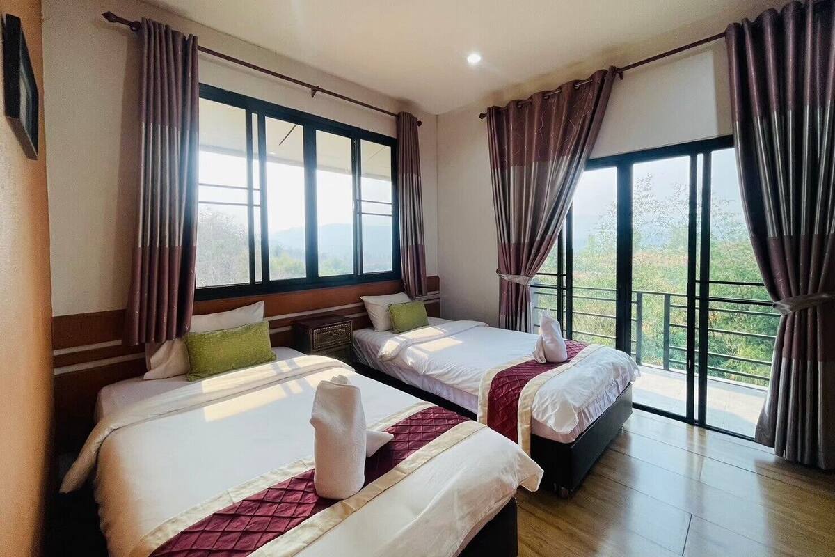 Ein Hotelzimmer mit zwei Betten, großen Fenstern und Vorhängen.